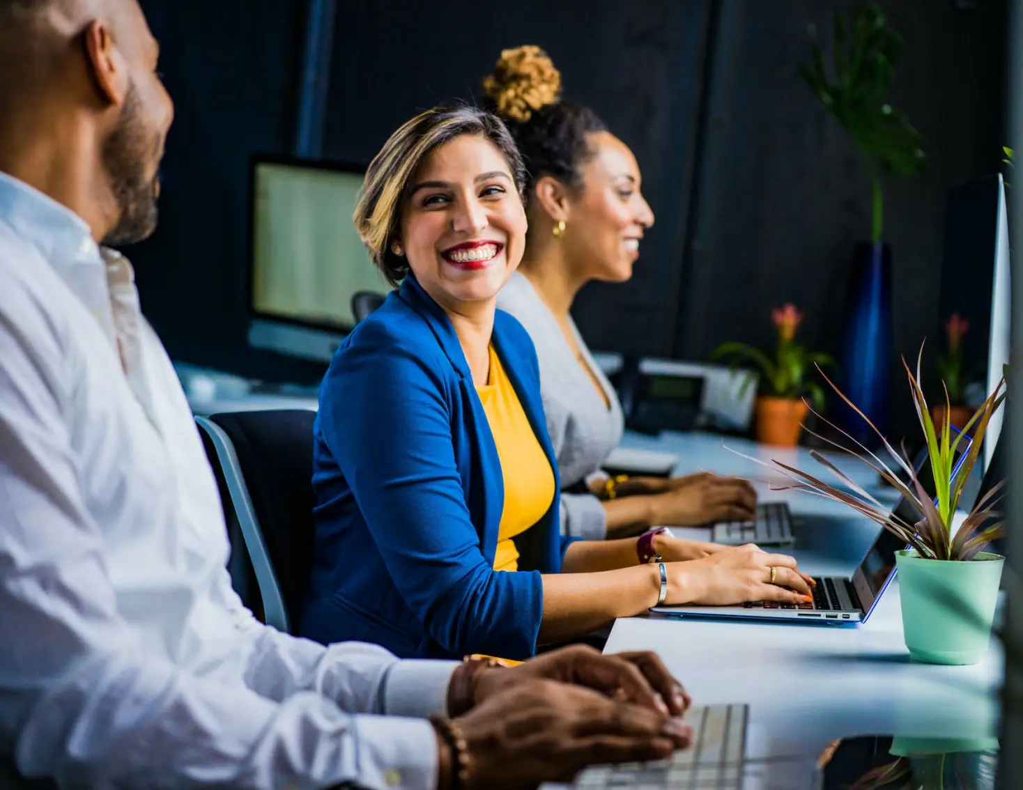 Woman in blue blazer in front of laptop laughing with colleague